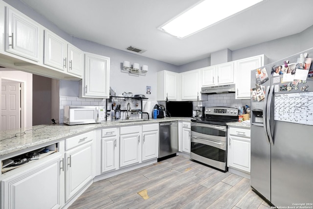 kitchen with sink, light hardwood / wood-style flooring, appliances with stainless steel finishes, light stone counters, and white cabinets