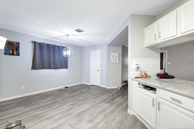 kitchen featuring white cabinets, decorative backsplash, hanging light fixtures, light stone countertops, and light hardwood / wood-style flooring