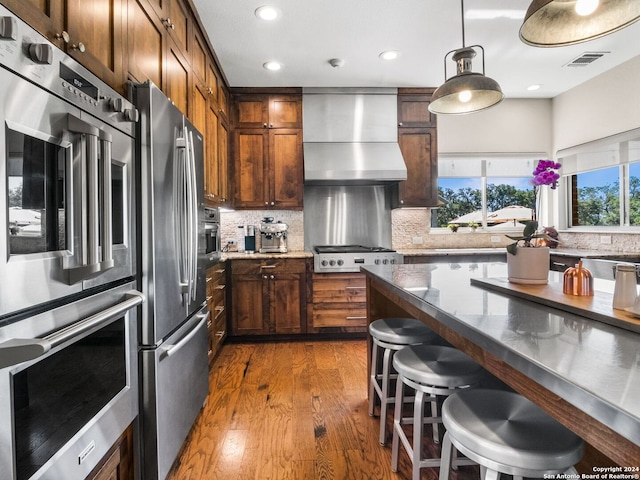 kitchen featuring wall chimney exhaust hood, dark stone countertops, appliances with stainless steel finishes, backsplash, and dark wood-type flooring