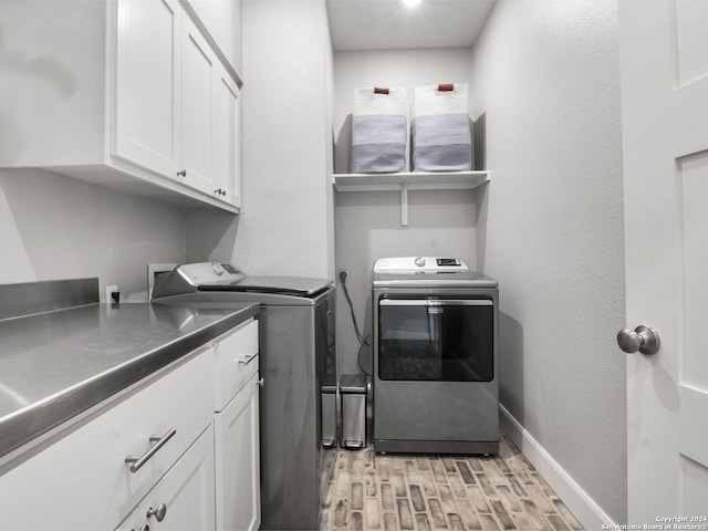 laundry room featuring washing machine and clothes dryer, cabinets, and light hardwood / wood-style floors