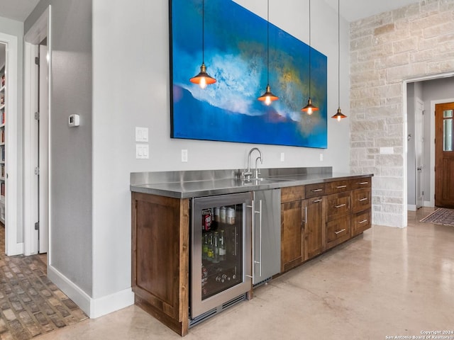 bar with sink, decorative light fixtures, stainless steel counters, and beverage cooler