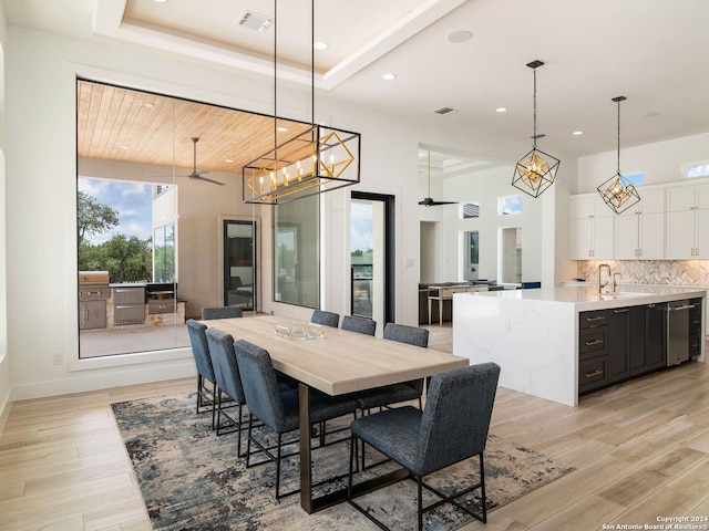 dining area with light hardwood / wood-style floors, sink, a high ceiling, a raised ceiling, and a notable chandelier