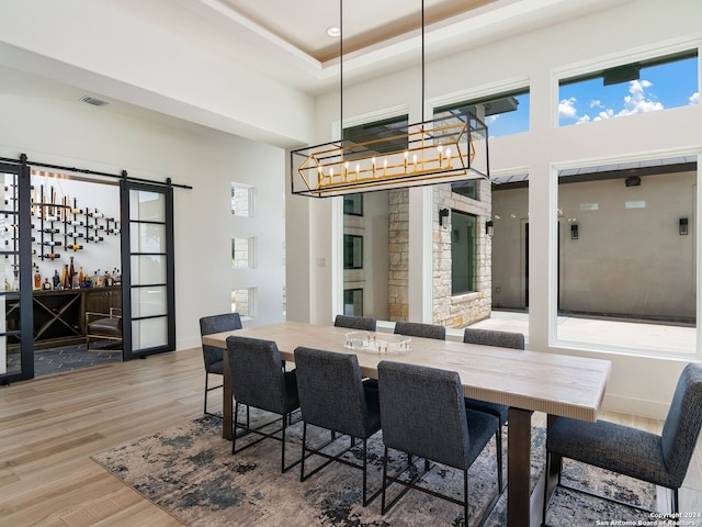 dining room with a raised ceiling, a chandelier, a barn door, a high ceiling, and hardwood / wood-style flooring