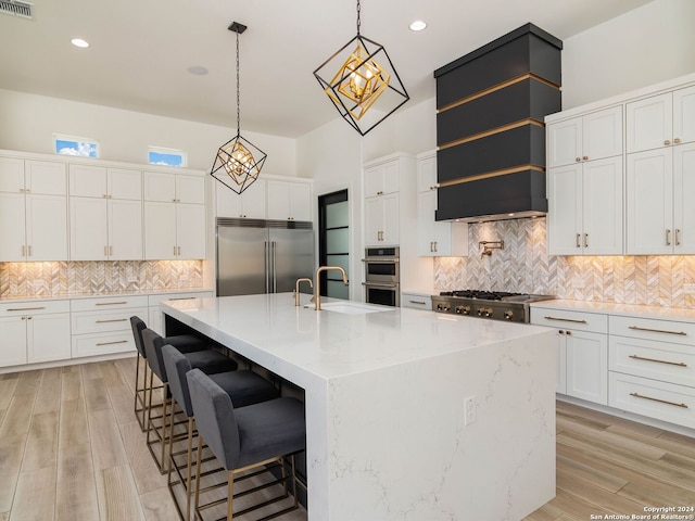 kitchen with appliances with stainless steel finishes, backsplash, light hardwood / wood-style floors, a spacious island, and sink