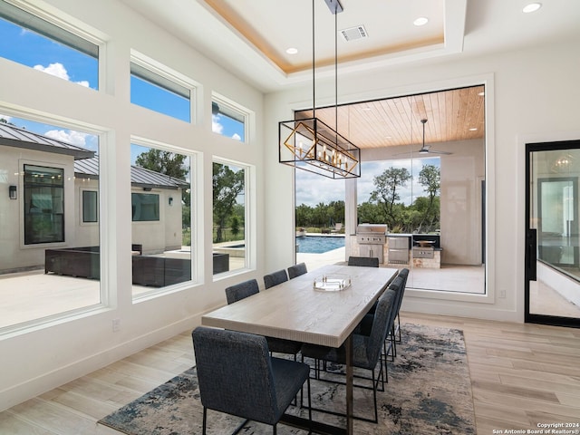 dining area with ceiling fan with notable chandelier, light hardwood / wood-style flooring, and a raised ceiling