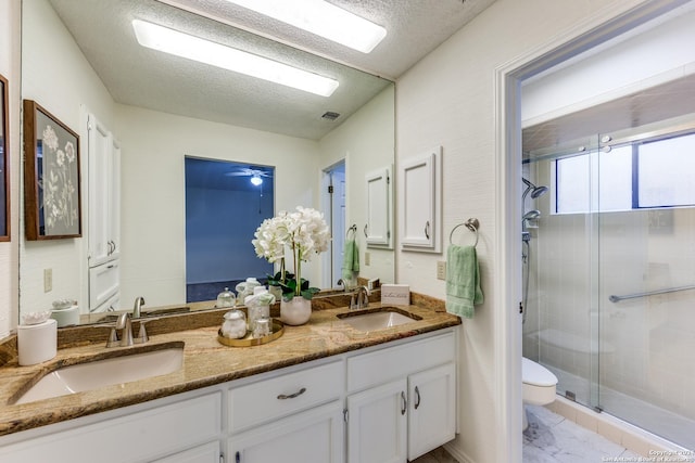 bathroom featuring a textured ceiling, ceiling fan, toilet, a shower with door, and vanity