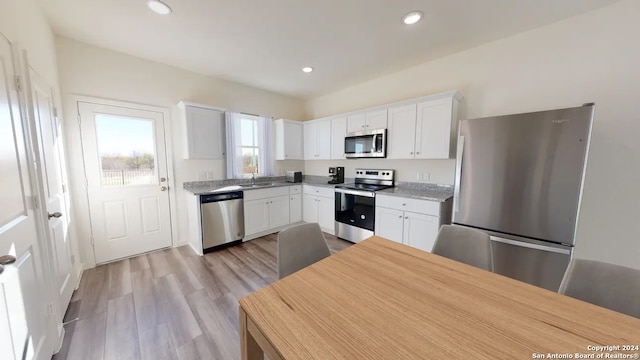 kitchen with light hardwood / wood-style flooring, stainless steel appliances, sink, light stone counters, and white cabinetry