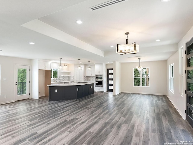 unfurnished living room with a raised ceiling, an inviting chandelier, and dark hardwood / wood-style flooring