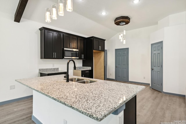 kitchen featuring lofted ceiling with beams, an island with sink, sink, hanging light fixtures, and light hardwood / wood-style floors