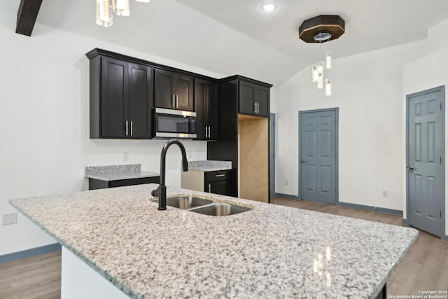 kitchen featuring lofted ceiling, sink, hanging light fixtures, light wood-type flooring, and a kitchen island with sink