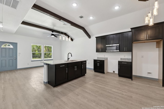 kitchen with sink, hanging light fixtures, lofted ceiling with beams, an island with sink, and light wood-type flooring