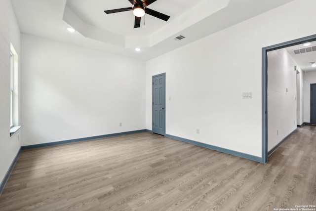 spare room featuring a tray ceiling, ceiling fan, and light wood-type flooring