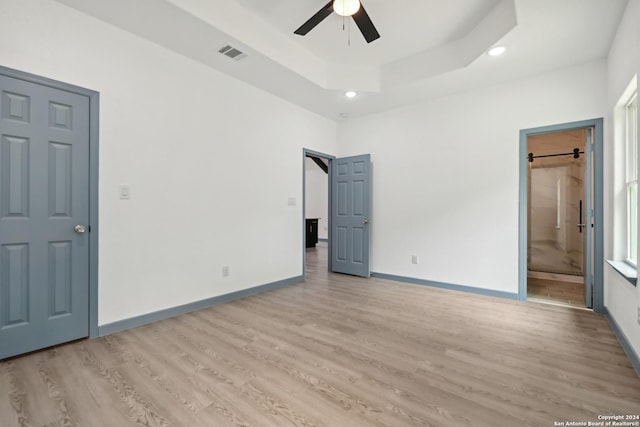 unfurnished bedroom with ceiling fan, connected bathroom, a raised ceiling, and light hardwood / wood-style flooring