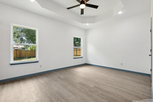 spare room featuring a raised ceiling, ceiling fan, and light hardwood / wood-style floors