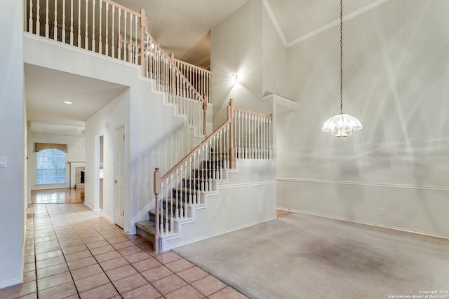 stairs with a notable chandelier, tile patterned floors, and a towering ceiling