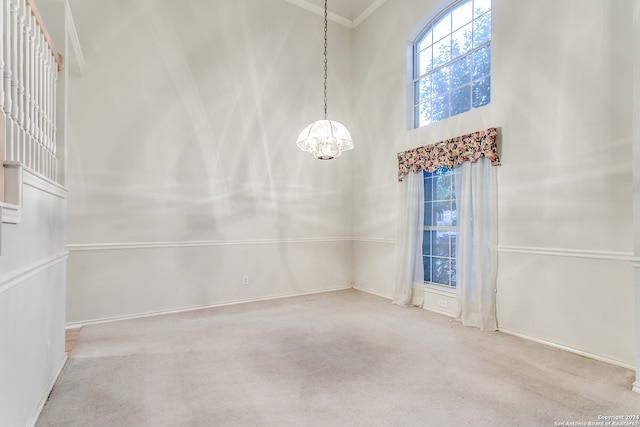 spare room with ornamental molding, a chandelier, light carpet, and a towering ceiling