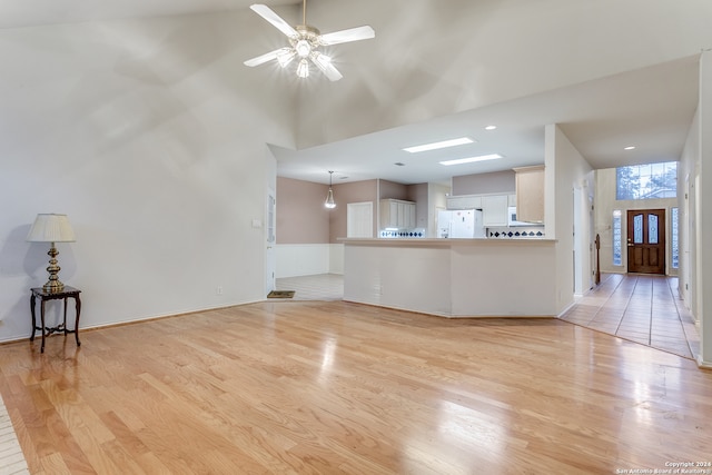 unfurnished living room with a towering ceiling, light wood-type flooring, and ceiling fan