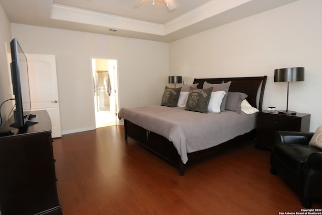 bedroom with ceiling fan, a tray ceiling, hardwood / wood-style flooring, and connected bathroom