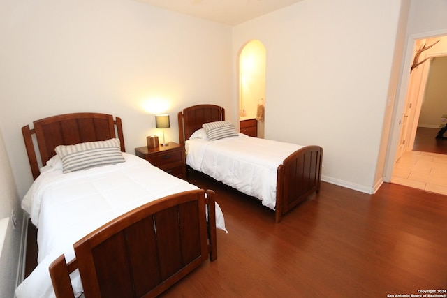 bedroom featuring connected bathroom, arched walkways, baseboards, and wood finished floors