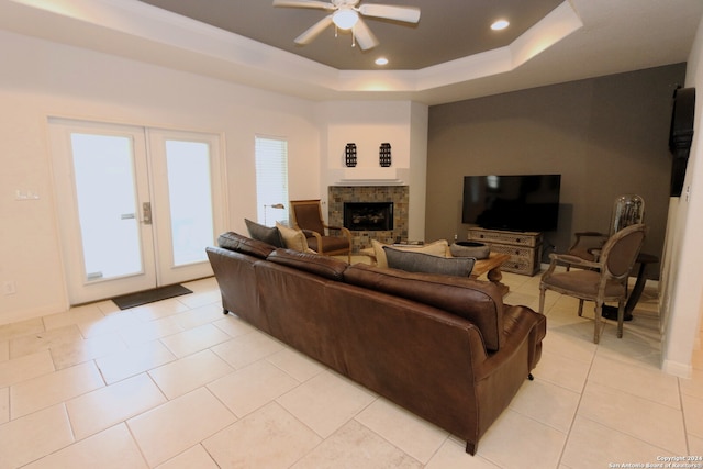 living room with a stone fireplace, a tray ceiling, ceiling fan, and light tile patterned floors