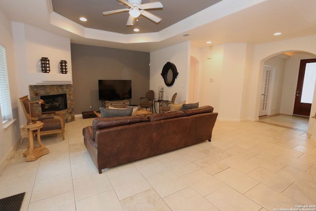 tiled living room featuring ceiling fan, a fireplace, a healthy amount of sunlight, and a tray ceiling