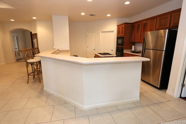 kitchen featuring light tile patterned flooring, kitchen peninsula, black appliances, and a kitchen bar