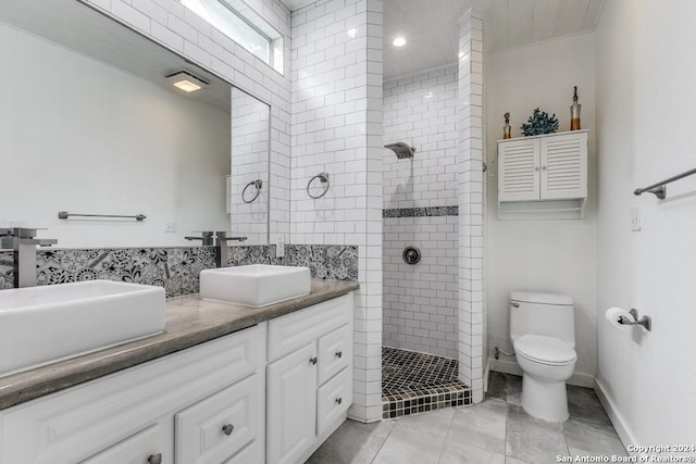 bathroom with toilet, tile patterned flooring, tiled shower, and vanity