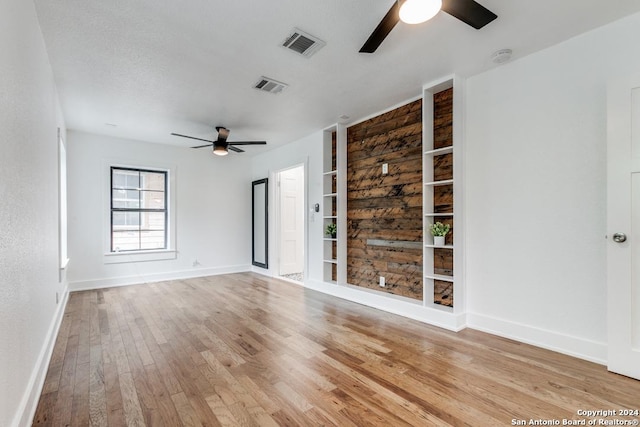 empty room featuring ceiling fan, light hardwood / wood-style flooring, and built in shelves