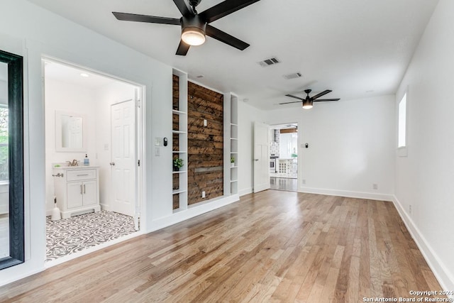 empty room featuring ceiling fan, light wood-type flooring, built in features, and a healthy amount of sunlight