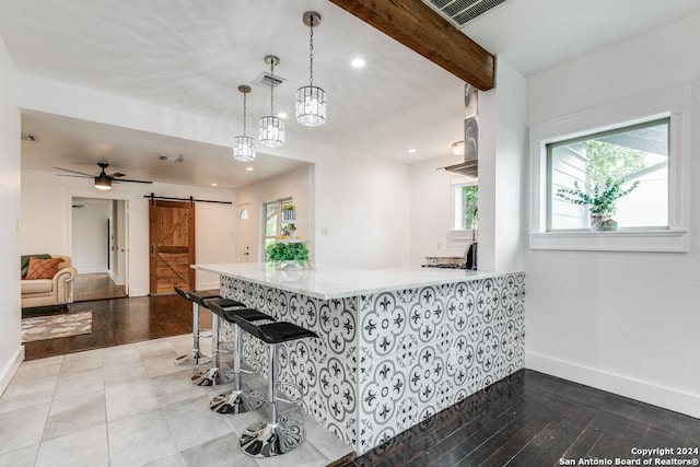 kitchen featuring decorative light fixtures, a barn door, hardwood / wood-style floors, beam ceiling, and kitchen peninsula