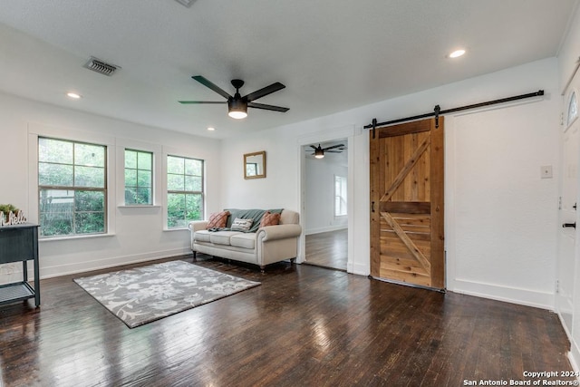 living room with ceiling fan, dark wood-type flooring, and a barn door