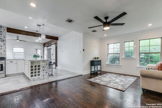 living room with light hardwood / wood-style floors, a barn door, ceiling fan, a textured ceiling, and beam ceiling