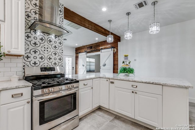 kitchen with a barn door, kitchen peninsula, island exhaust hood, stainless steel gas range, and white cabinets