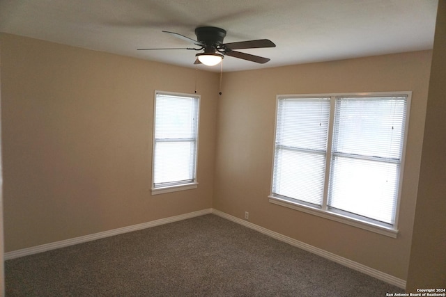 spare room featuring ceiling fan, dark carpet, and a healthy amount of sunlight