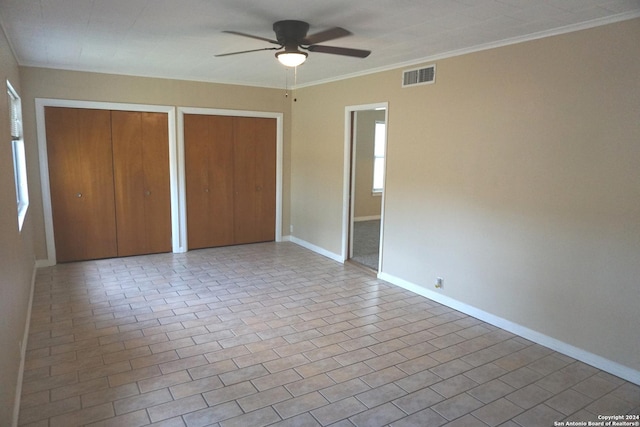 unfurnished bedroom featuring ceiling fan, ornamental molding, and multiple closets