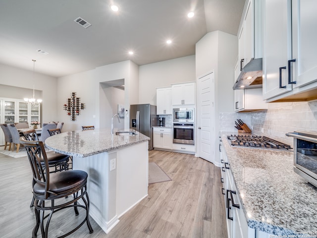 kitchen featuring appliances with stainless steel finishes, white cabinetry, a kitchen island with sink, and wall chimney exhaust hood