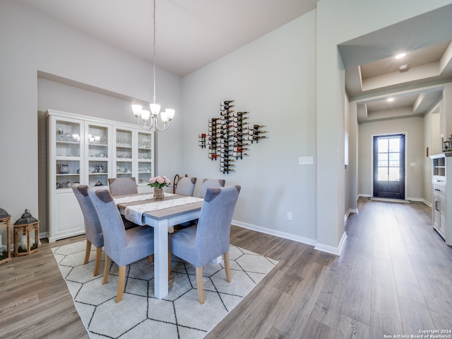 dining space with light wood-type flooring, a tray ceiling, and a notable chandelier