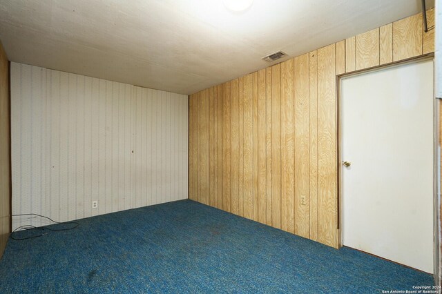 carpeted empty room featuring wood walls