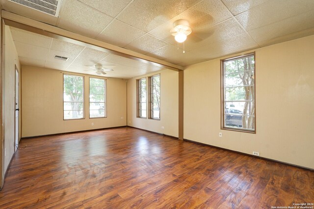 empty room featuring hardwood / wood-style flooring, a drop ceiling, ceiling fan, and plenty of natural light