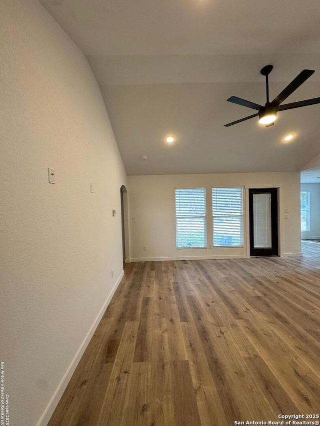 unfurnished living room with a ceiling fan, vaulted ceiling, baseboards, arched walkways, and wood finished floors