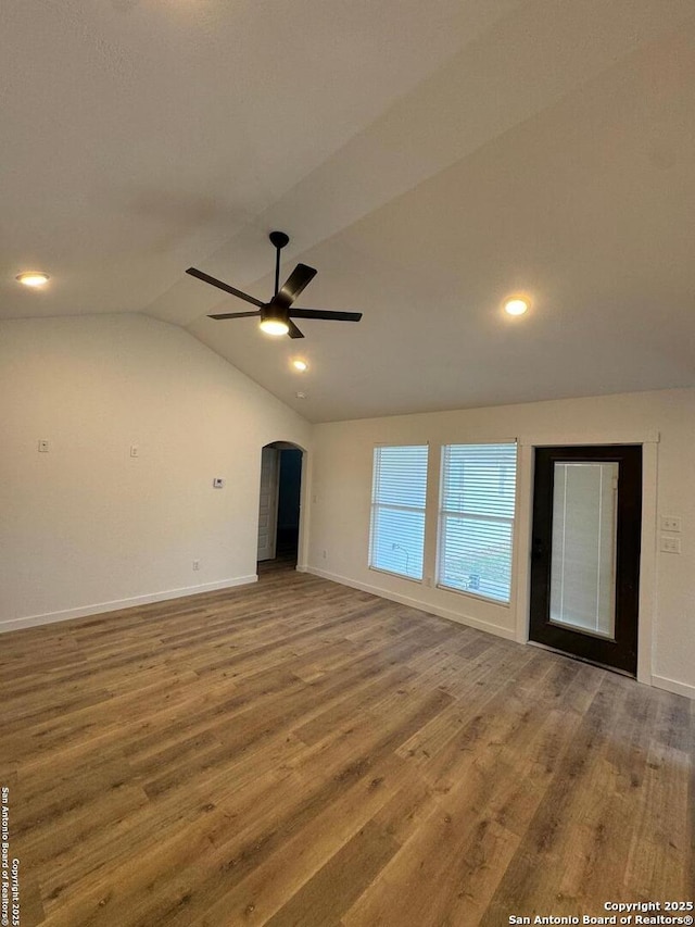 empty room with lofted ceiling, wood finished floors, baseboards, and arched walkways