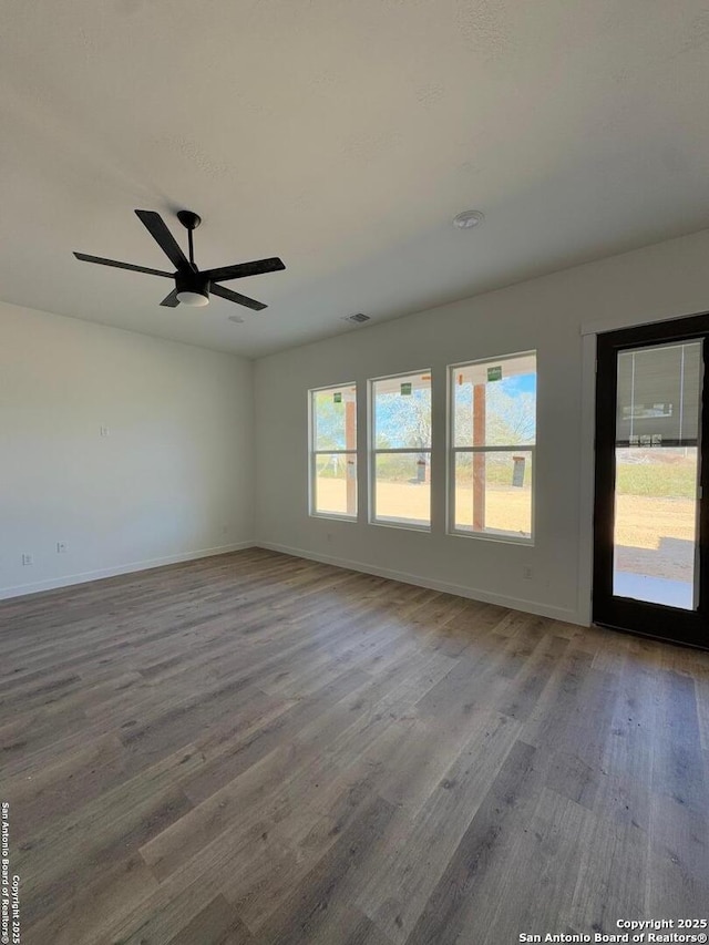 empty room featuring a ceiling fan, visible vents, baseboards, and wood finished floors