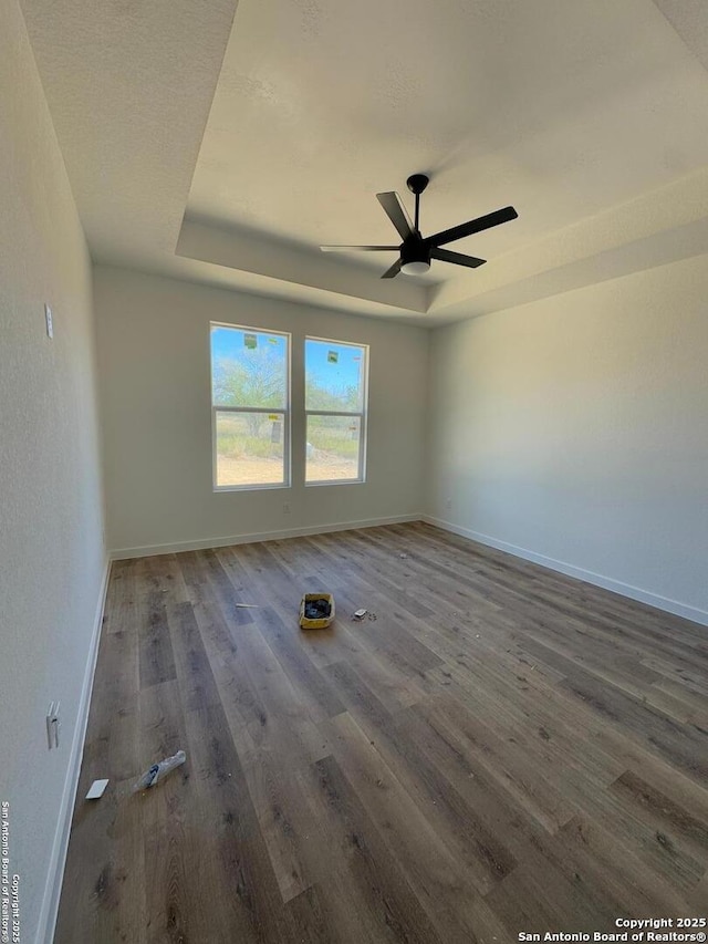 empty room with dark wood-type flooring, ceiling fan, and a tray ceiling