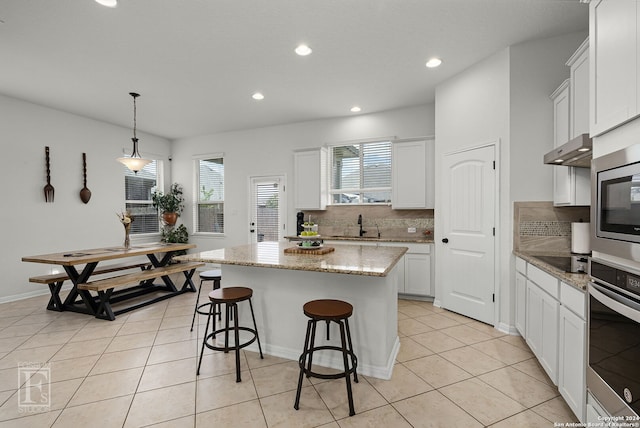 kitchen featuring pendant lighting, white cabinets, decorative backsplash, a kitchen island, and stainless steel appliances