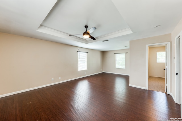 spare room with plenty of natural light, dark wood-type flooring, a raised ceiling, and ceiling fan