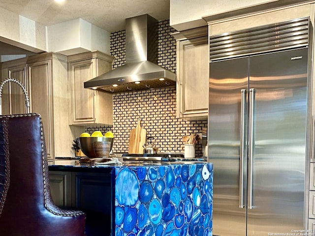 kitchen featuring built in refrigerator, backsplash, and wall chimney exhaust hood