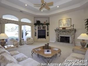 living room featuring carpet floors, a fireplace, ceiling fan, and a raised ceiling