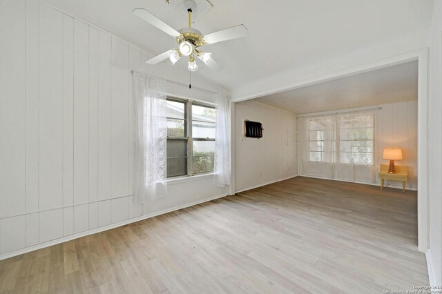 unfurnished room with vaulted ceiling, wooden walls, ceiling fan, and light hardwood / wood-style floors