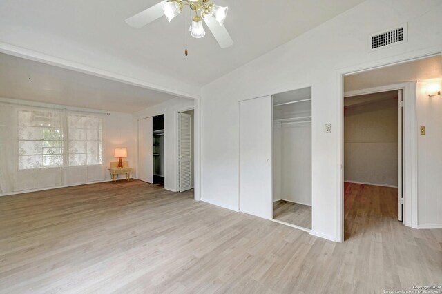 unfurnished bedroom with lofted ceiling, ceiling fan, multiple closets, and light wood-type flooring