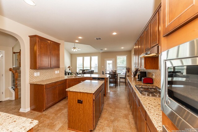 kitchen with sink, light stone counters, a kitchen island, kitchen peninsula, and backsplash